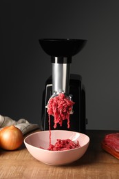 Photo of Electric meat grinder with beef mince and onion on wooden table against grey background