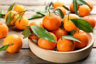 Photo of Fresh ripe tangerines with green leaves on wooden table, closeup