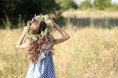 Photo of Little girl wearing wreath made of beautiful flowers in field on sunny day