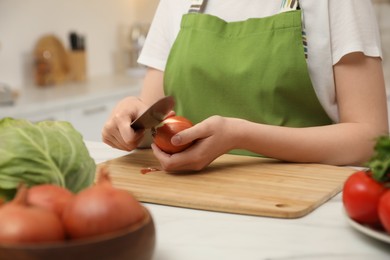 Photo of Woman peeling onion at table in kitchen, closeup. Preparing vegetable