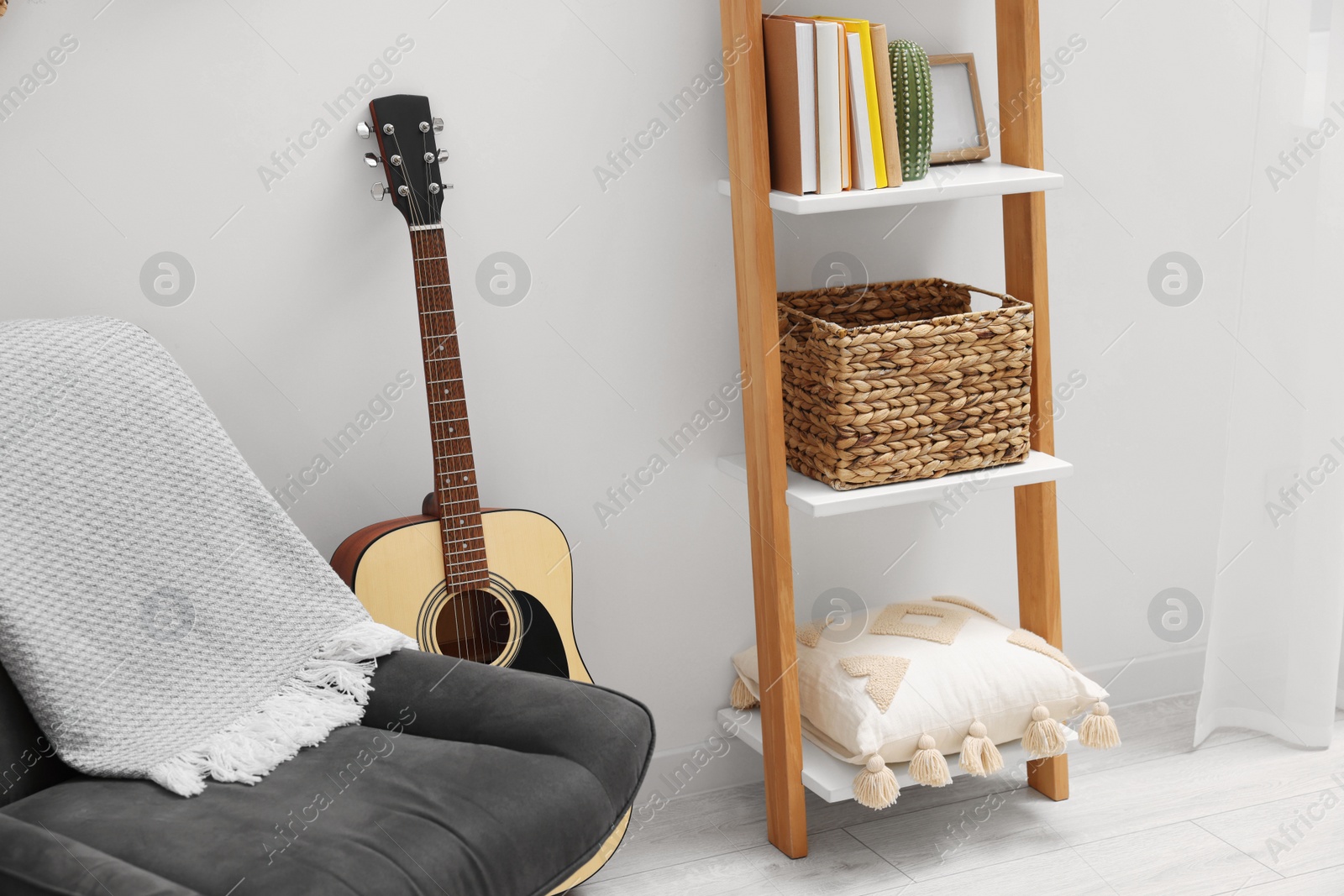 Photo of Spring atmosphere. Wooden shelving unit, acoustic guitar and comfortable chair in stylish room