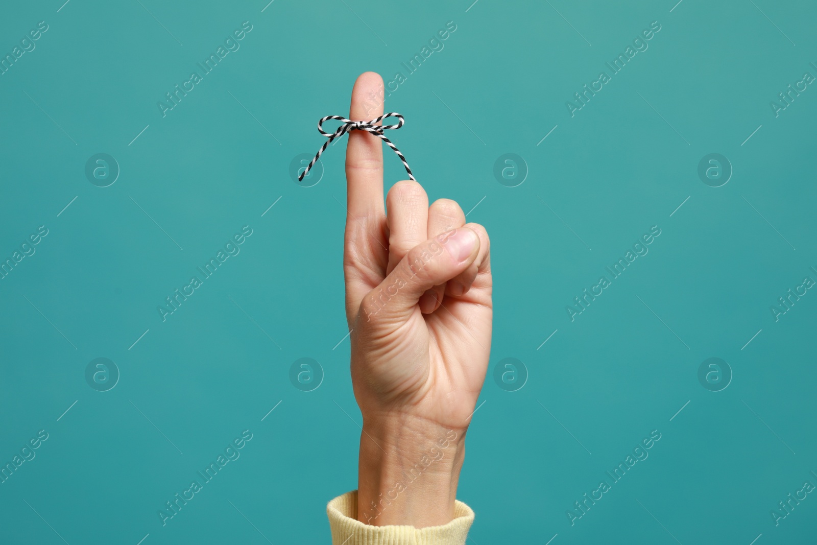 Photo of Woman showing index finger with tied bow as reminder on light blue background, closeup