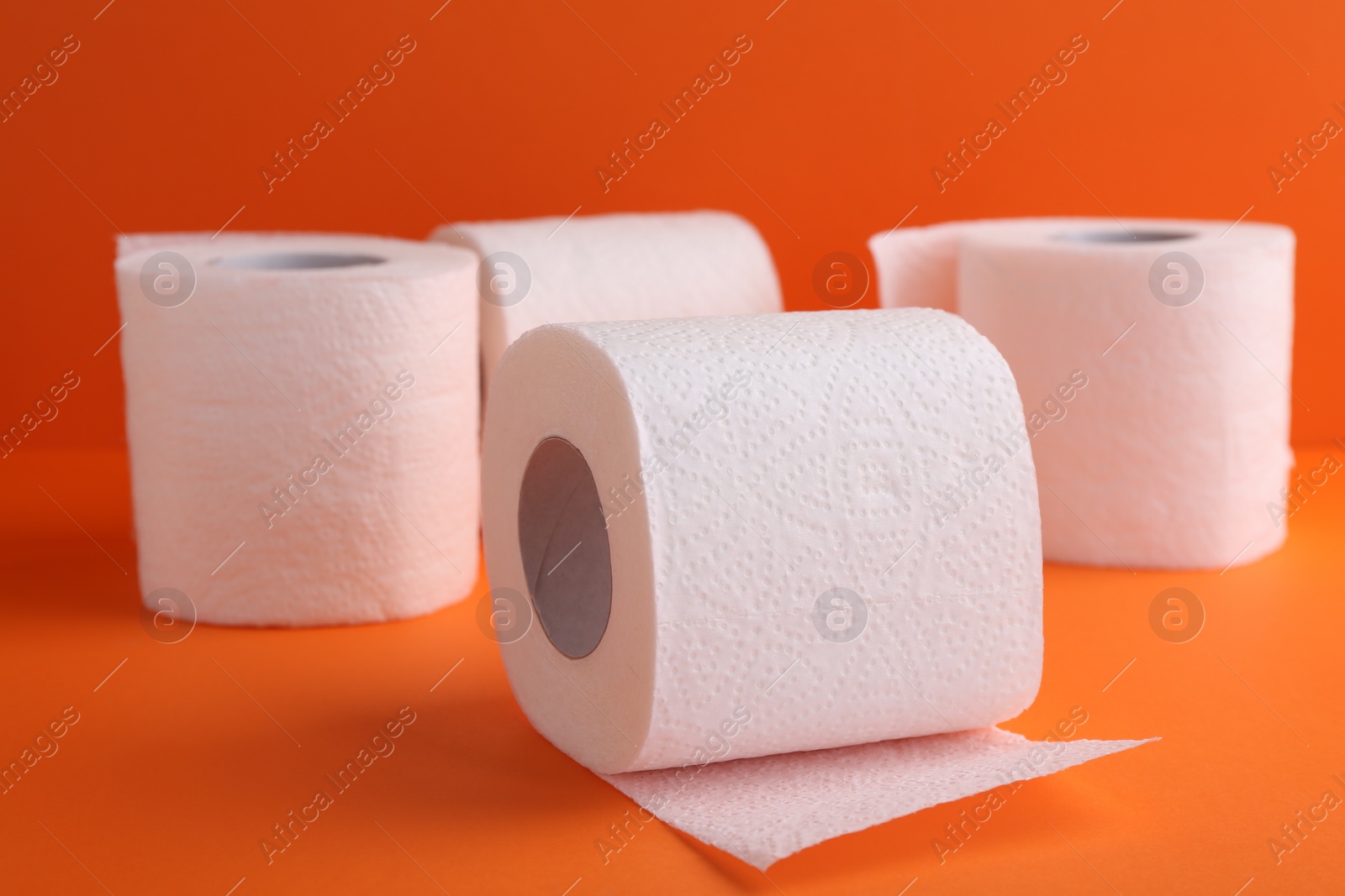 Photo of Soft toilet paper rolls on orange background, closeup