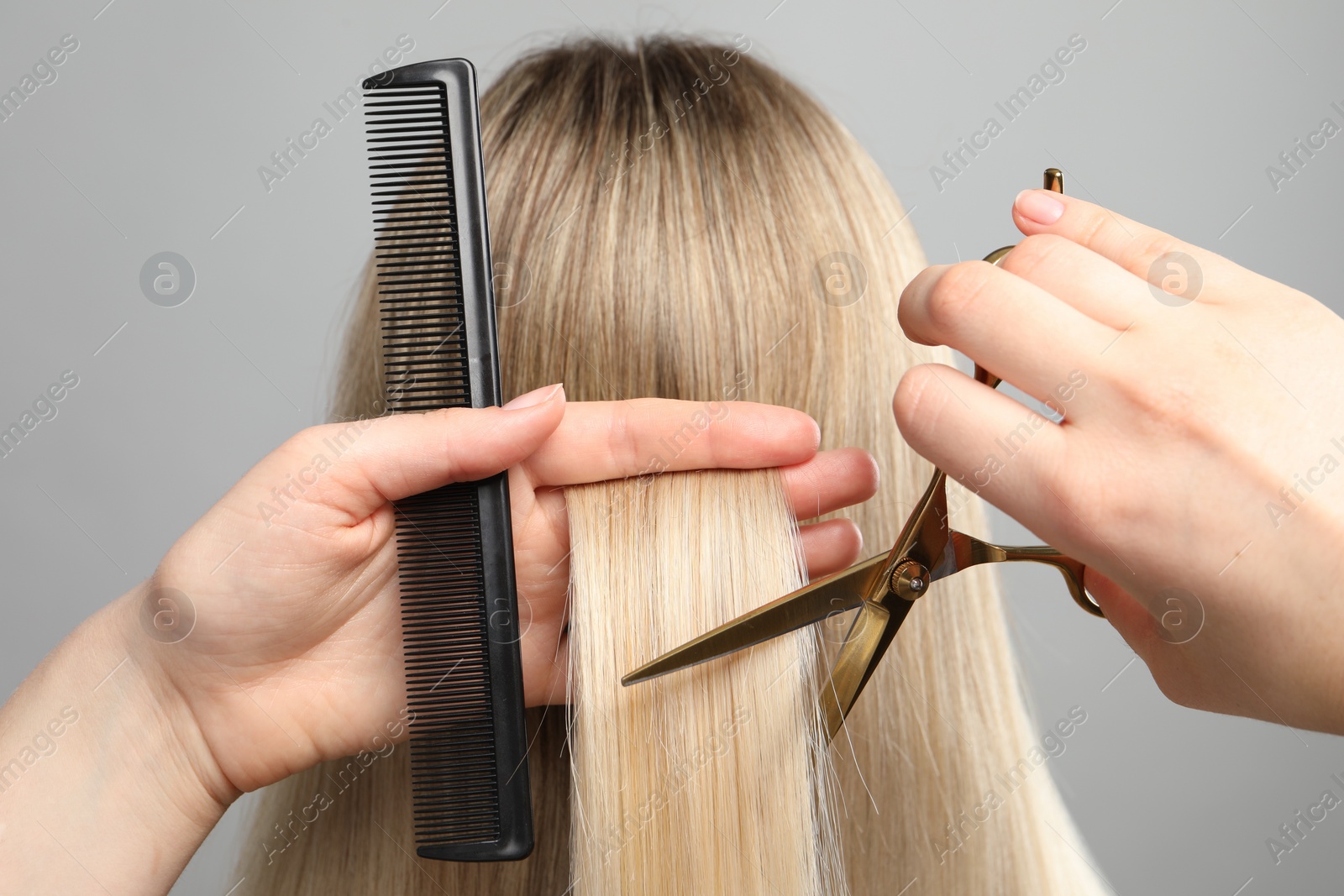 Photo of Hairdresser cutting client's hair with scissors on light grey background, closeup