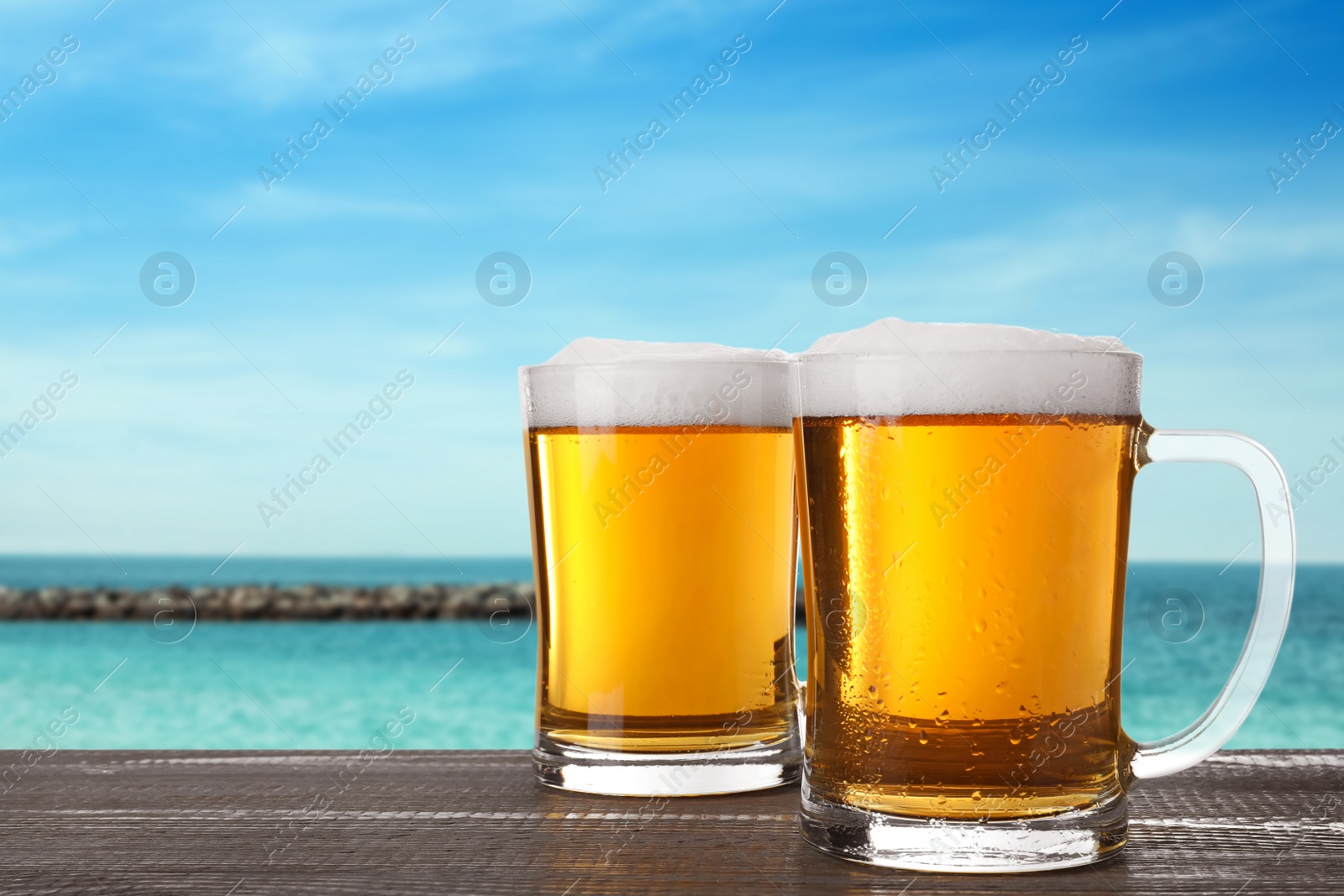 Image of Cold beer on wooden desk against blurred sea. Space for text