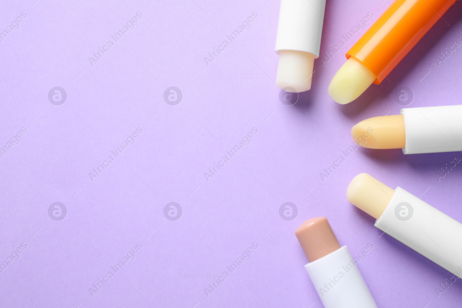 Photo of Hygienic lipsticks on lilac background, flat lay. Space for text