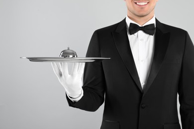 Photo of Butler holding metal tray with service bell on grey background, closeup