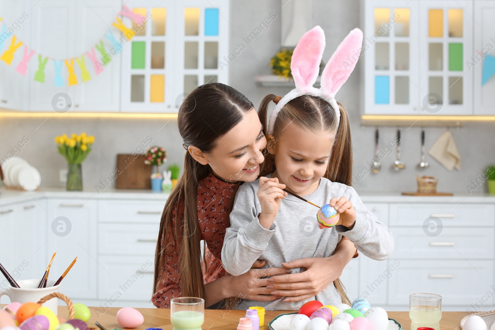 Photo of Mother and her cute daughter painting Easter eggs at table in kitchen