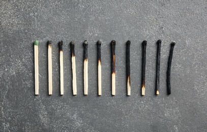Row of burnt matches and whole one on grey background, flat lay. Human life phases concept