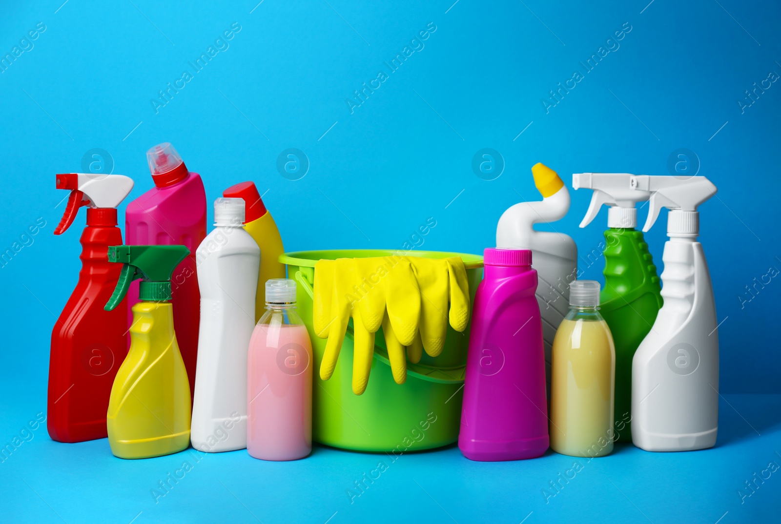 Photo of Green bucket, gloves and bottles of detergents on light blue background. Cleaning supplies