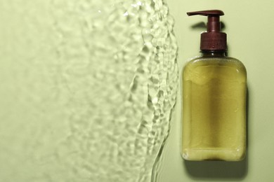 Photo of Bottle of facial cleanser in water against olive background, top view. Space for text