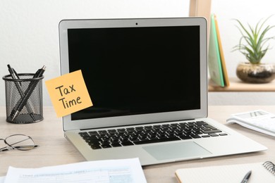 Reminder note with words Tax Time and laptop on wooden table indoors