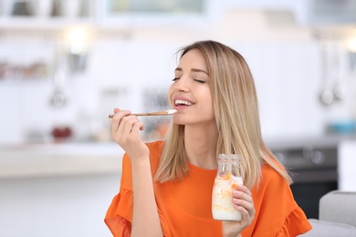 Photo of Young attractive woman eating tasty yogurt in kitchen