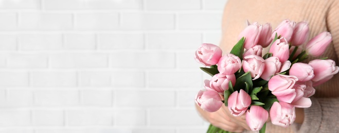 Image of Woman with beautiful pink spring tulips near white brick wall, space for text. Horizontal banner design