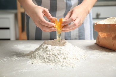 Woman breaking egg over pile of flour on table in kitchen