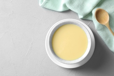 Photo of Bowl of condensed milk served on grey table, top view with space for text. Dairy products