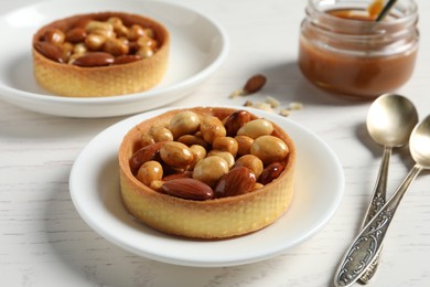 Photo of Tartlets with caramelized nuts on white wooden table, closeup. Tasty dessert