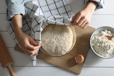 Woman covering dough with napkin at white wooden table, top view