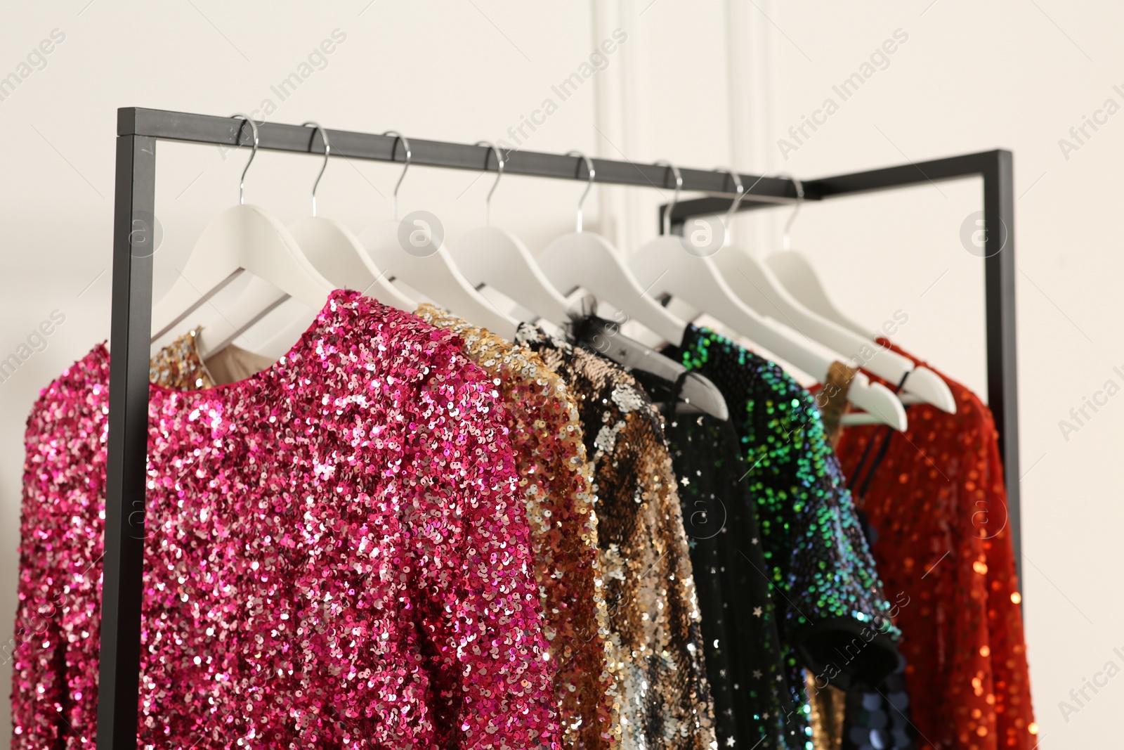 Photo of Clothing rack with colorful sequin party dresses on hangers near white wall indoors, closeup