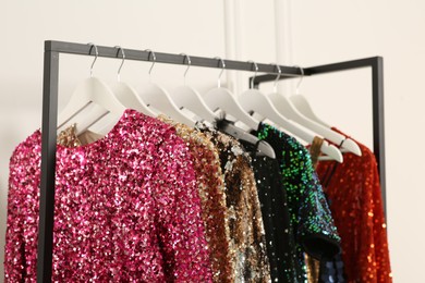 Photo of Clothing rack with colorful sequin party dresses on hangers near white wall indoors, closeup