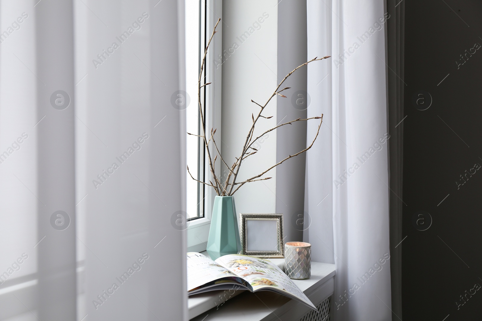 Photo of Tree twigs in ceramic vase, decor and magazine on window sill at home