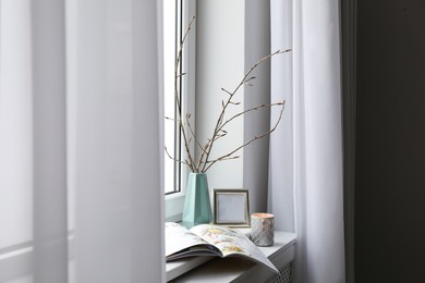 Photo of Tree twigs in ceramic vase, decor and magazine on window sill at home