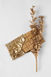 Shiny stylish gold chocolate bar and branch with leaves on white background, top view