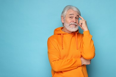 Senior man with mustache on light blue background, space for text