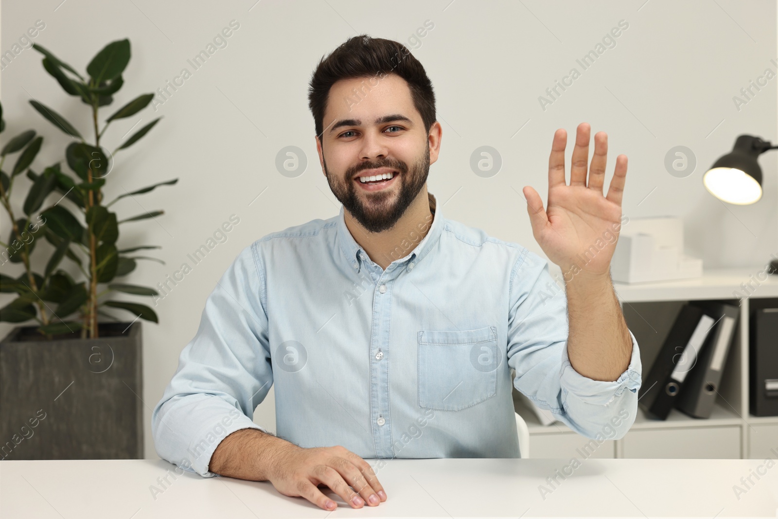 Photo of Happy young man waving hello during video chat indoors, view from web camera