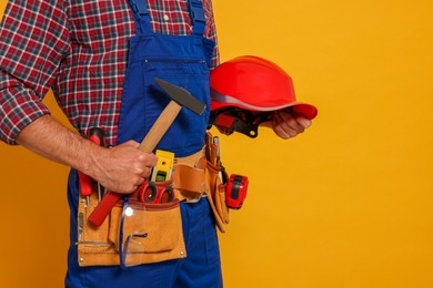 Professional builder in uniform with hammer and tool belt on yellow background, closeup