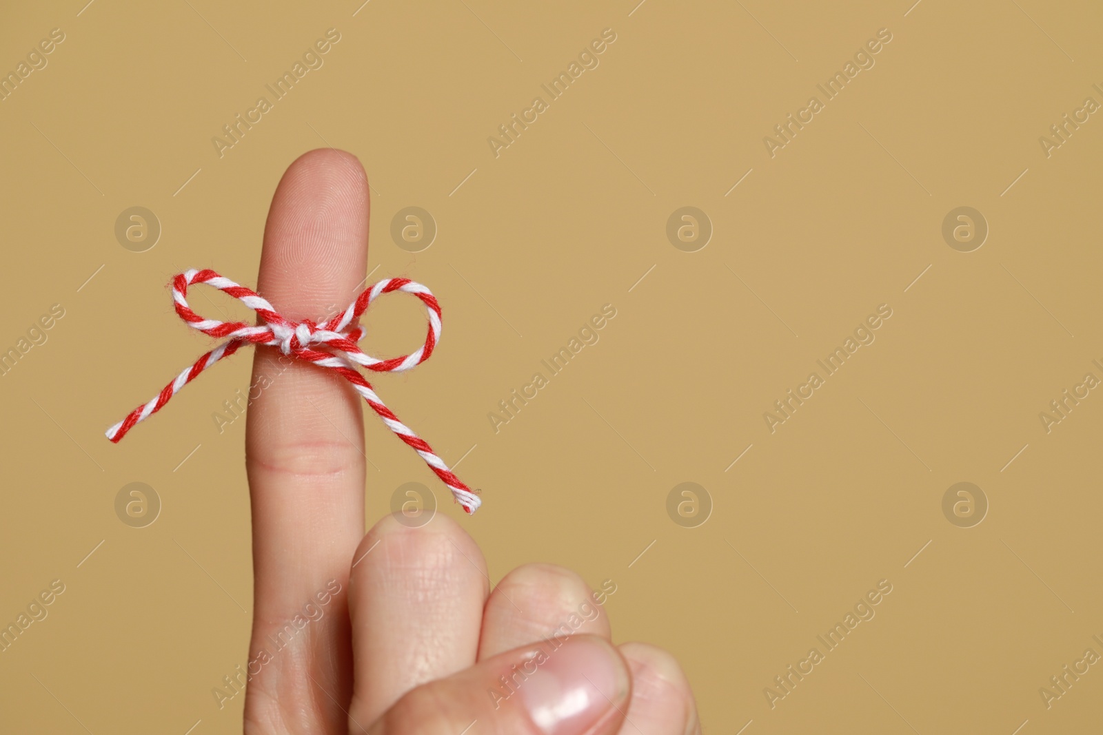 Photo of Woman showing index finger with tied bow as reminder on light brown background, closeup. Space for text