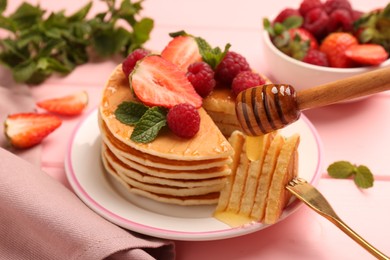 Photo of Dripping honey onto delicious pancakes with fresh berries on pink table, closeup