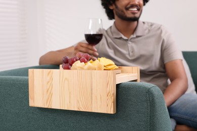 Photo of Grapes and snacks on sofa armrest wooden table. Man holding glass of wine at home, closeup