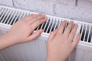 Photo of Girl warming hands on heating radiator indoors, closeup