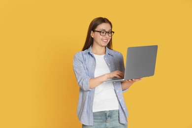 Young woman with modern laptop on yellow background