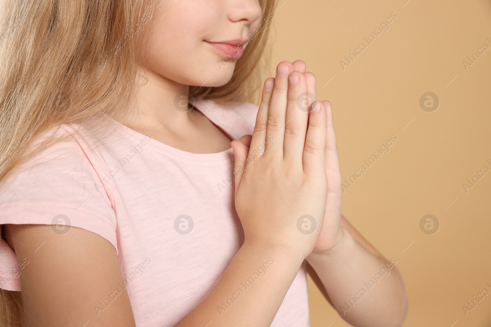 Photo of Girl with clasped hands praying on beige background, closeup