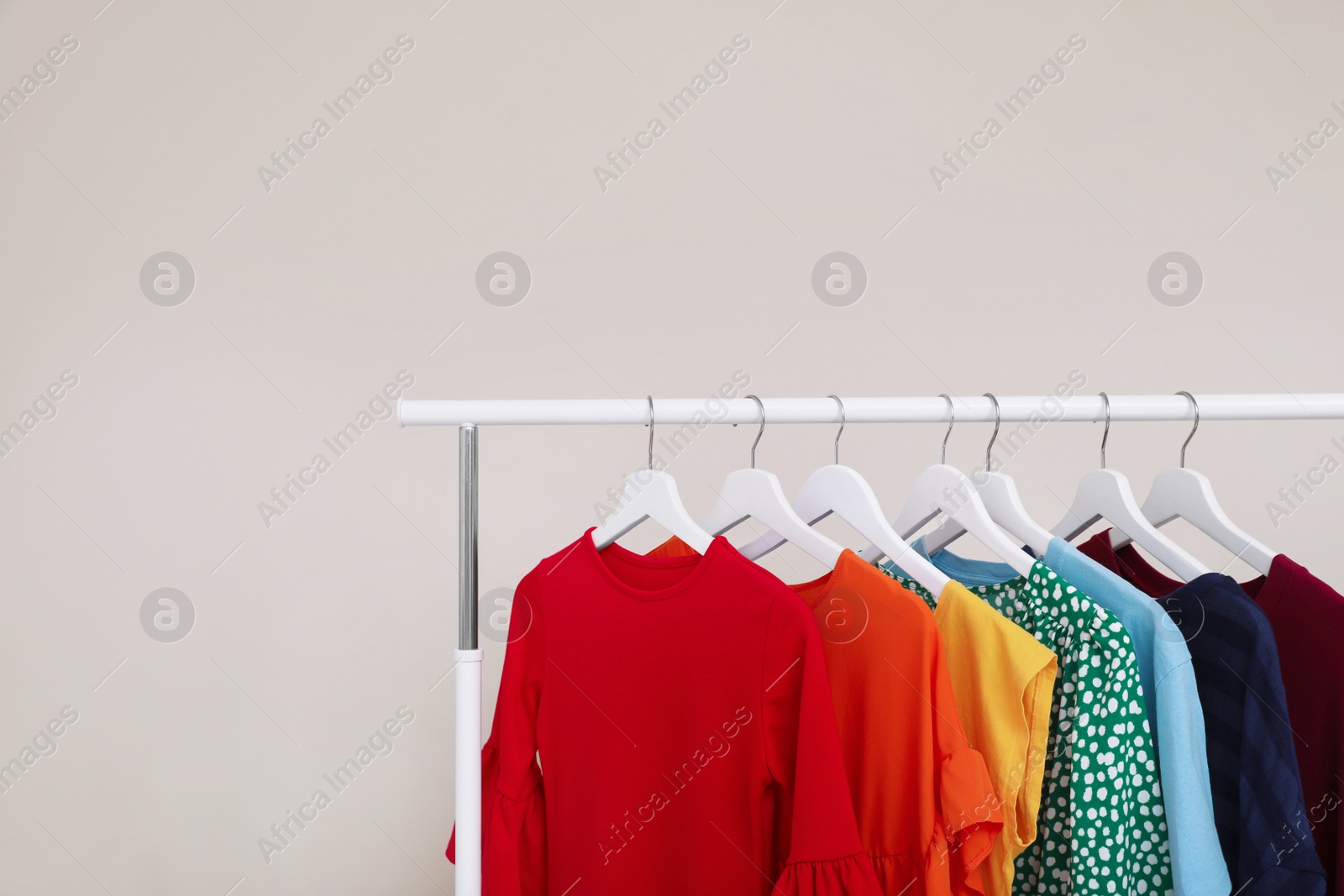 Photo of Wardrobe rack with different bright clothes on light background. Space for text