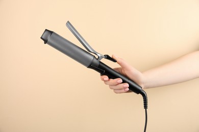 Photo of Hair styling appliance. Woman holding curling iron on beige background, closeup
