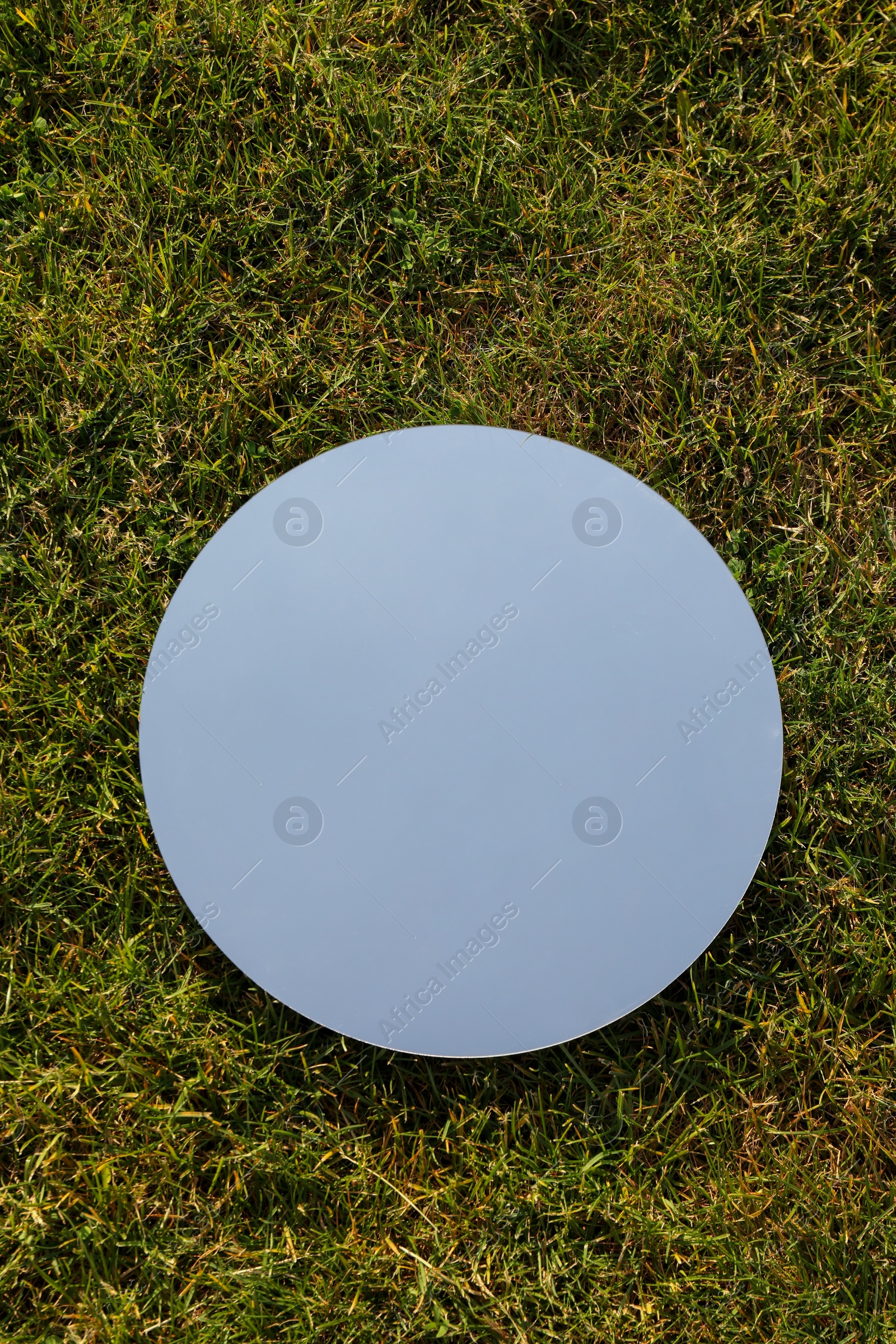 Photo of Spring atmosphere. Round mirror on grass reflecting sky, top view