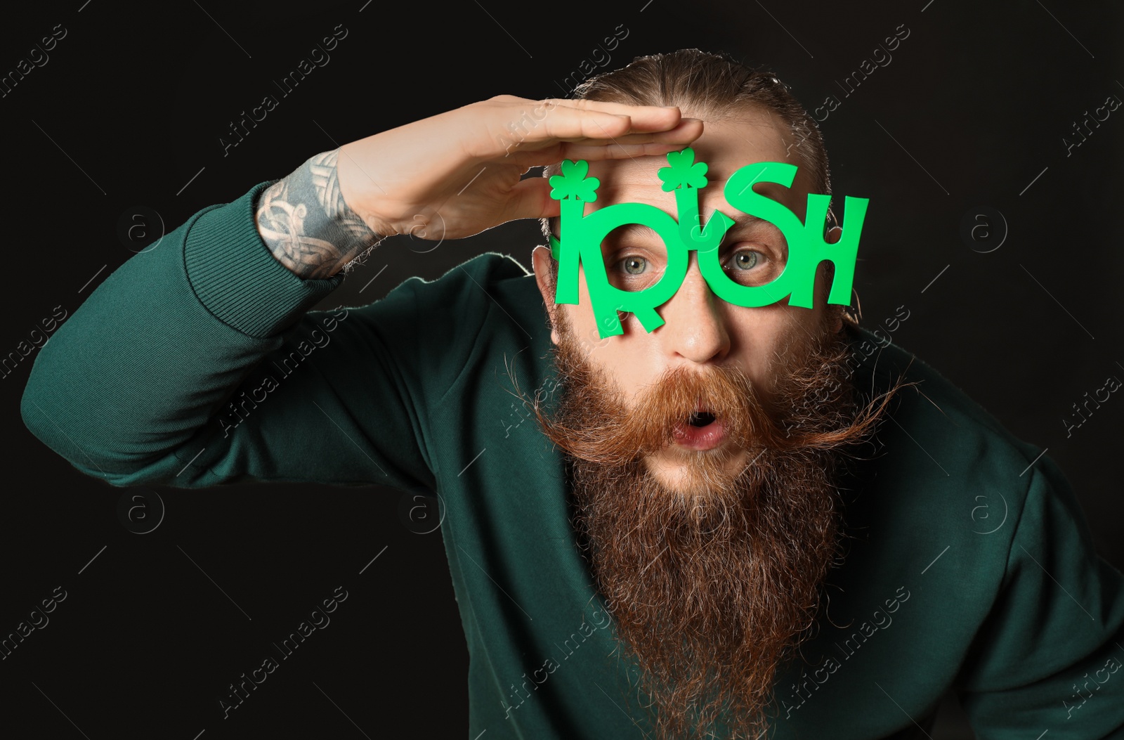 Photo of Bearded man in party glasses on black background. St. Patrick's Day celebration