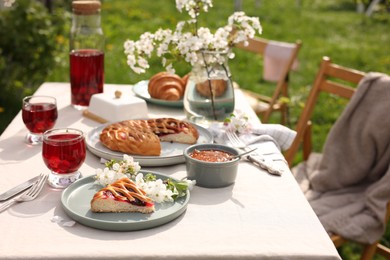 Photo of Stylish table setting with beautiful spring flowers, fruit drink and pie in garden