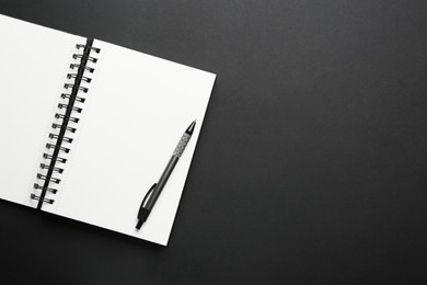 Photo of Notebook and pen on black background, top view. Space for text