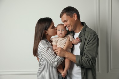 Happy family. Couple with their cute baby near light wall