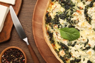 Photo of Delicious homemade spinach quiche, spices and knife on wooden table, flat lay