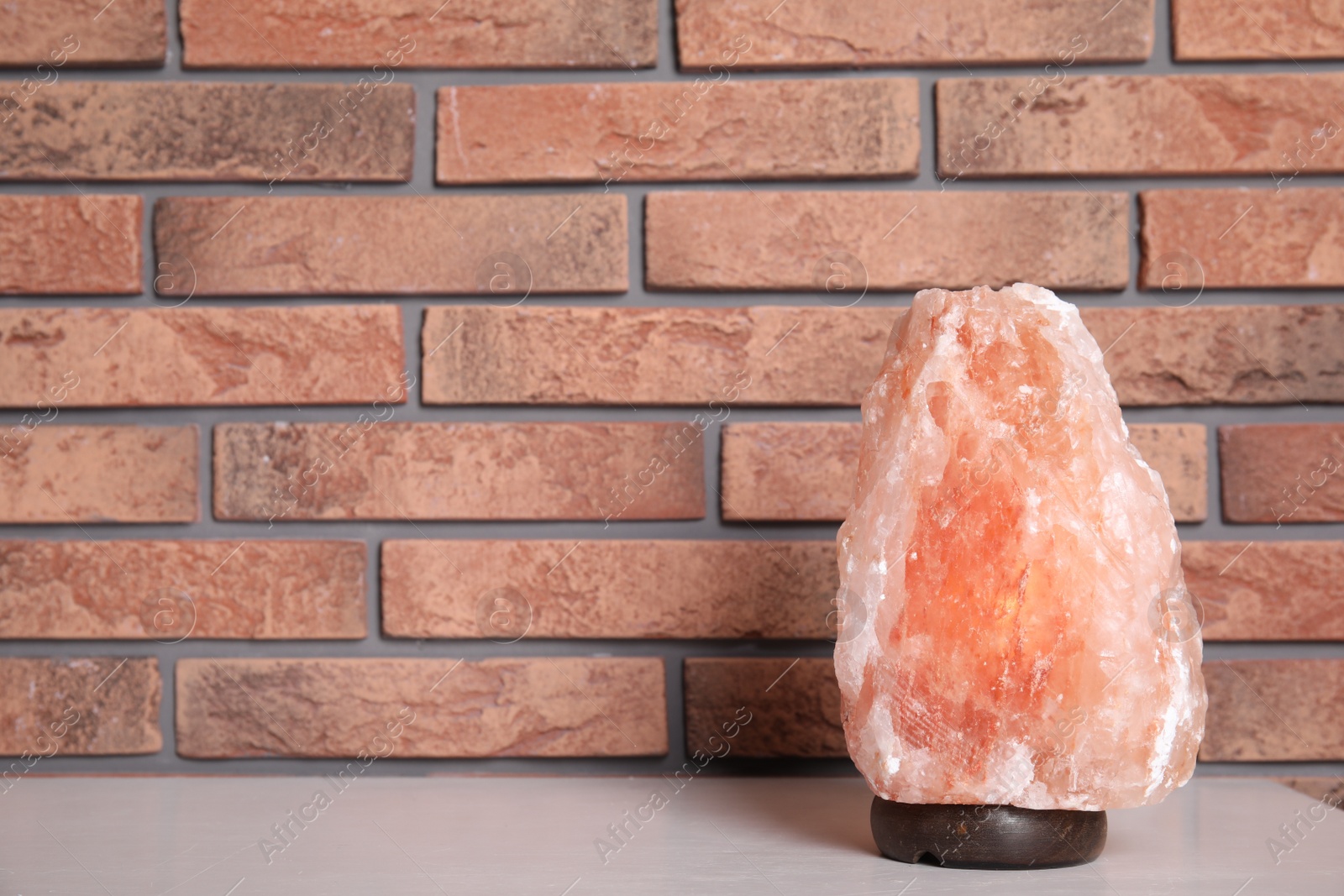 Photo of Himalayan salt lamp on table near brick wall. Space for text