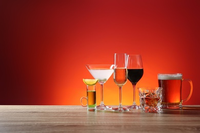 Photo of Different alcohol drinks on wooden table against red background. Space for text
