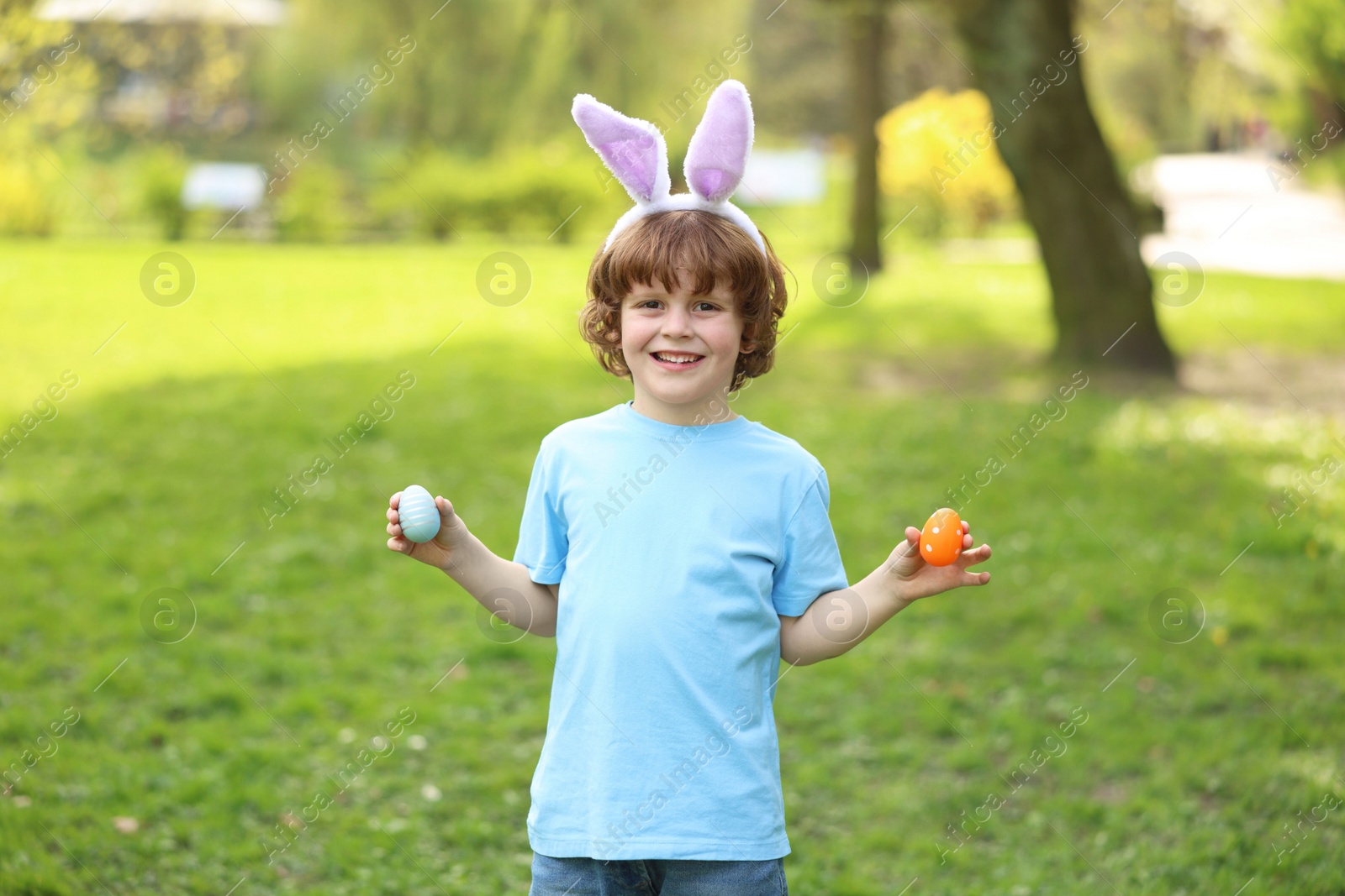 Photo of Easter celebration. Cute little boy in bunny ears holding painted eggs outdoors
