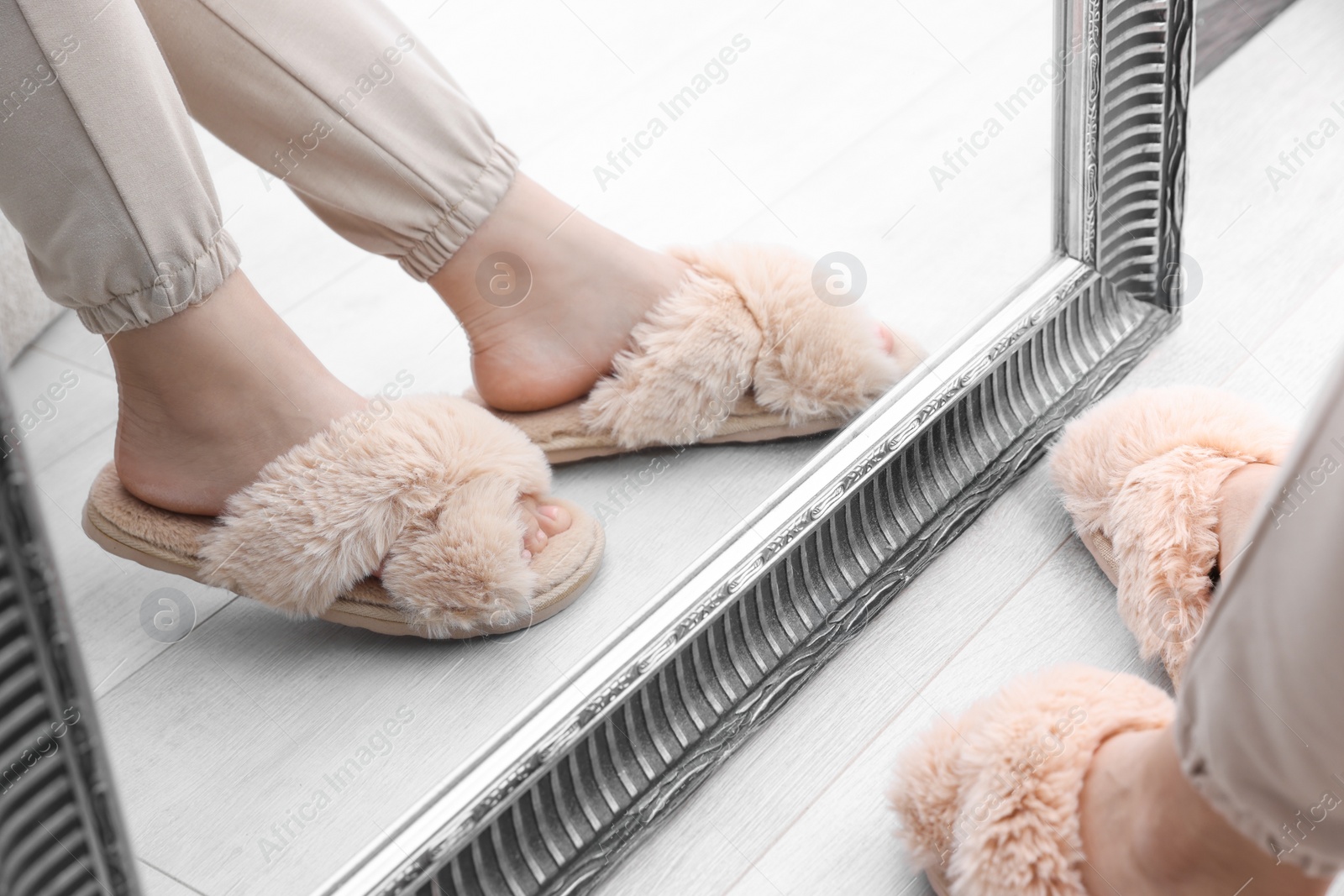 Photo of Woman wearing beige soft slippers near mirror, closeup