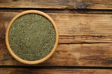 Photo of Bowl of dried dill on wooden table, top view. Space for text