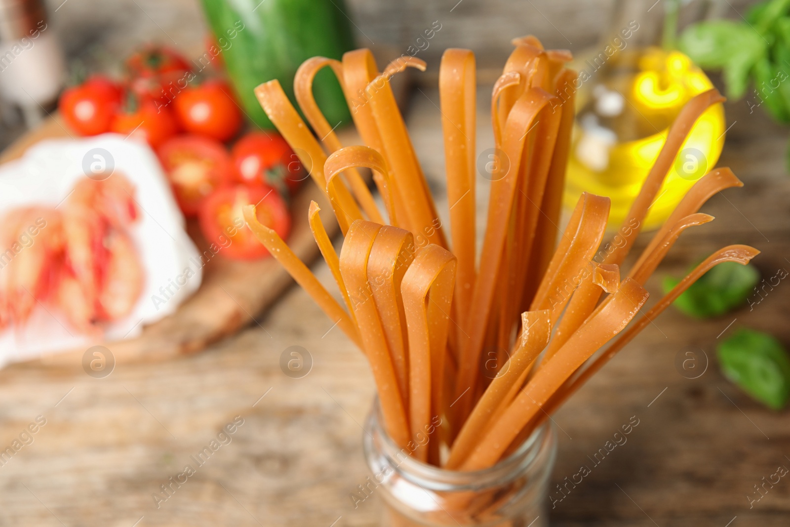 Photo of Jar with uncooked buckwheat noodles and fresh ingredients on wooden table, closeup